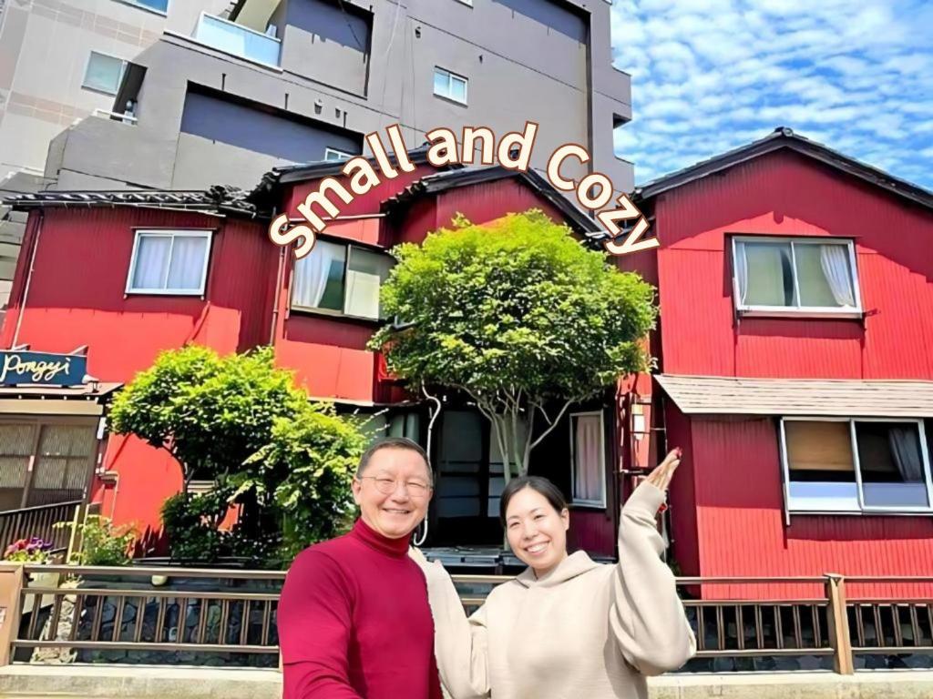 a man and woman standing in front of a red building at Guest House Pongyi in Kanazawa