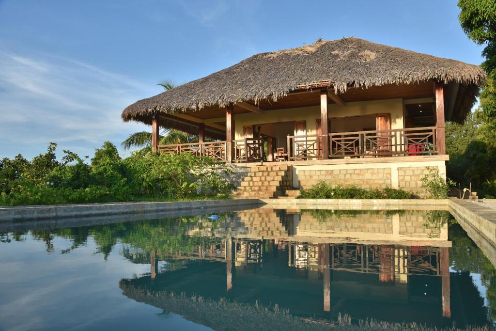 een huis met een rieten dak naast een waterlichaam bij Résidences-Bel-R in Nosy Be