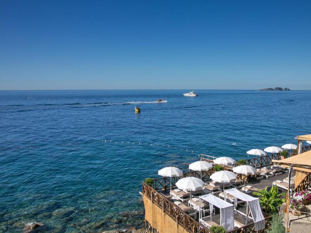 - une plage avec des parasols blancs et l'eau dans l'établissement Hotel Le Agavi, à Positano