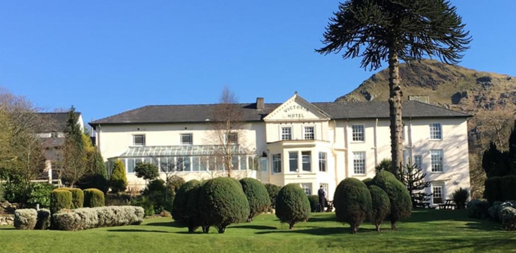 Une grande maison blanche avec des moutons dans la cour dans l'établissement Royal Victoria Hotel Snowdonia, à Llanberis