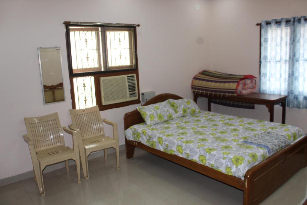 1 Schlafzimmer mit einem Bett, 2 Stühlen und einem Fenster in der Unterkunft Centaurus Homestay near Trichy Airport in Tiruchchirāppalli