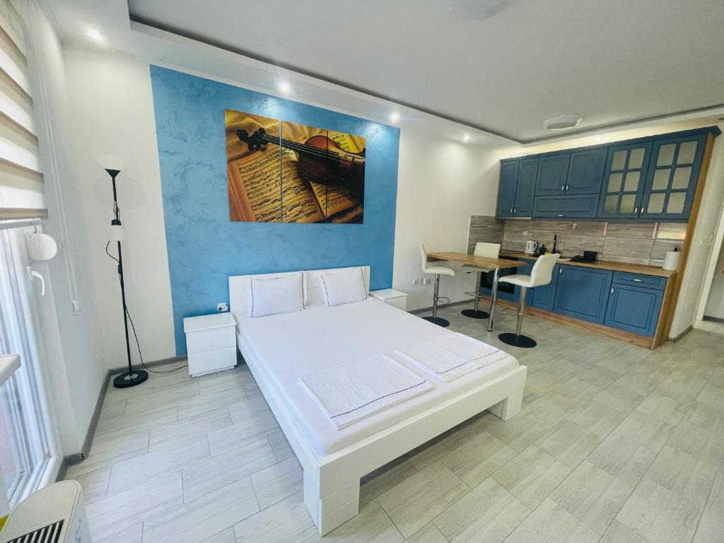 a bedroom with a white bed and a kitchen at Apartman Blue in Sombor