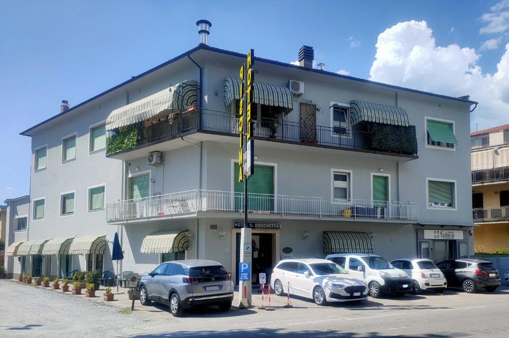 un grand bâtiment blanc avec des voitures garées dans un parking dans l'établissement Hotel Il Boschetto, à Pistoia