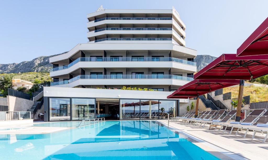 a hotel with a swimming pool and red umbrellas at Hotel Plaža Duće in Duće