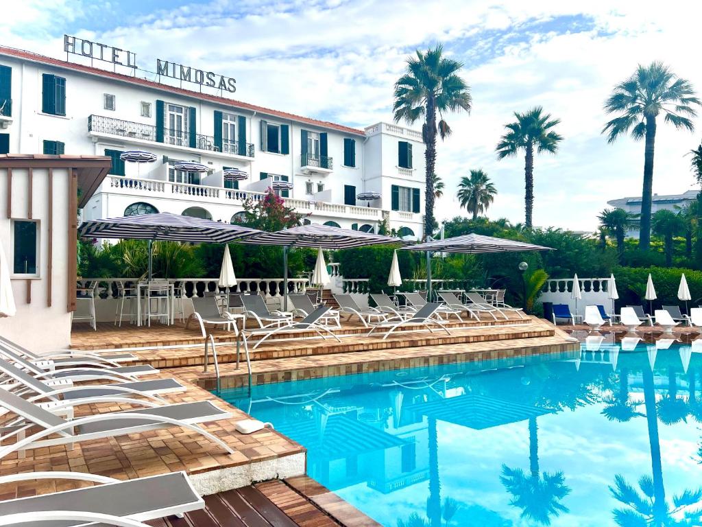 een hotel met een zwembad met stoelen en parasols bij Hotel des Mimosas in Juan-les-Pins