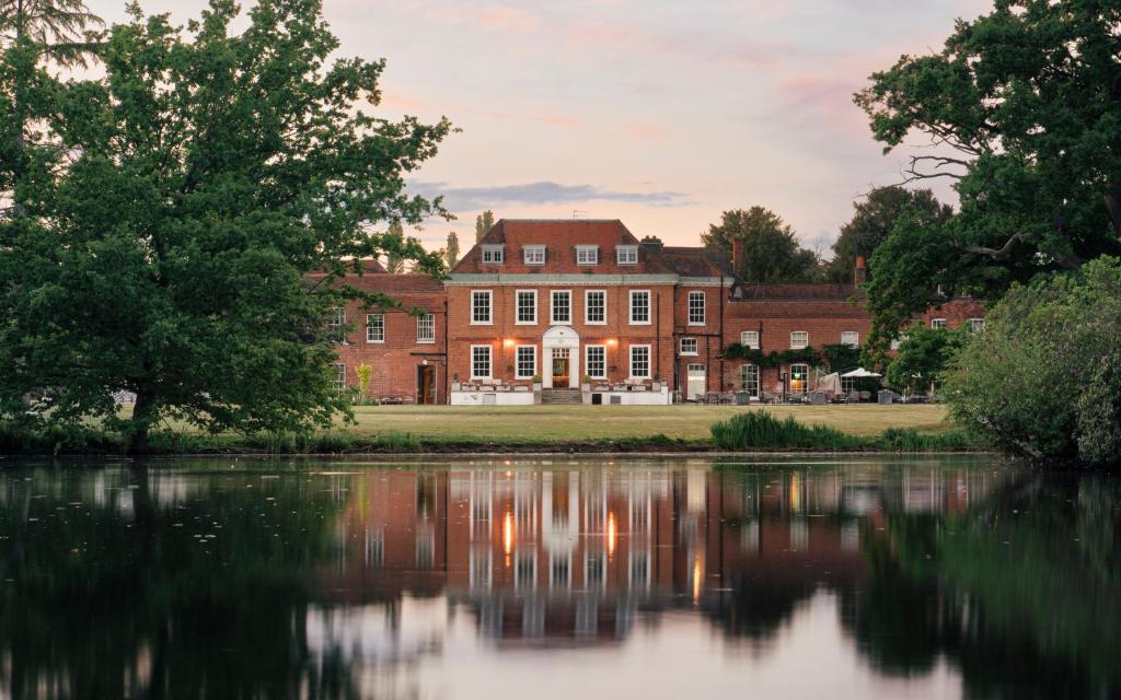 un gran edificio de ladrillo con reflejo en un lago en Stoke Place- Part of the Cairn Collection, en Slough