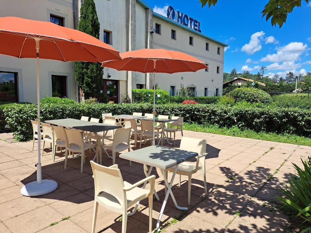 een tafel en stoelen met parasols voor een gebouw bij Hotel Le Saint Vincent Lyon Sud in Vourles