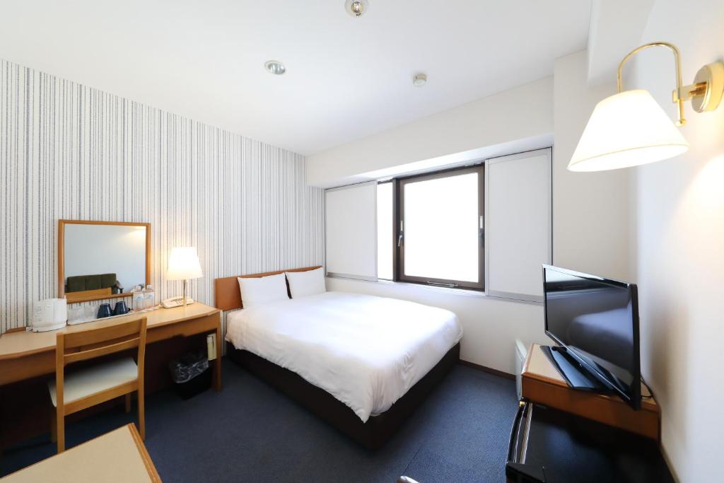 Cette chambre comprend un lit, un bureau et une télévision. dans l'établissement Smile Hotel Nihombashi Mitsukoshimae, à Tokyo