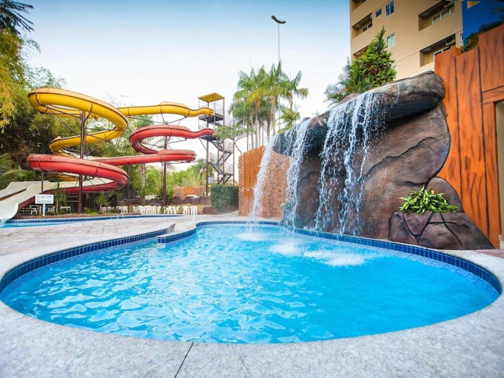 a water slide in a pool with a waterfall at ÁGUAS TERMAIS NATURAIS nas PISCINAS com ÁGUAS QUENTES 24 HORAS acesso GRÁTIS aos PARQUES AQUÁTICOS dos RESORTS GOLDEN DOLPHIN GRAND HOTEL do SUPREME e do EXPRESS os melhores HOTÉIS RESORTS com PARQUE AQUÁTICO em CALDAS NOVAS Garanta JÁ PROMOÇÃO QUALIDADE in Caldas Novas