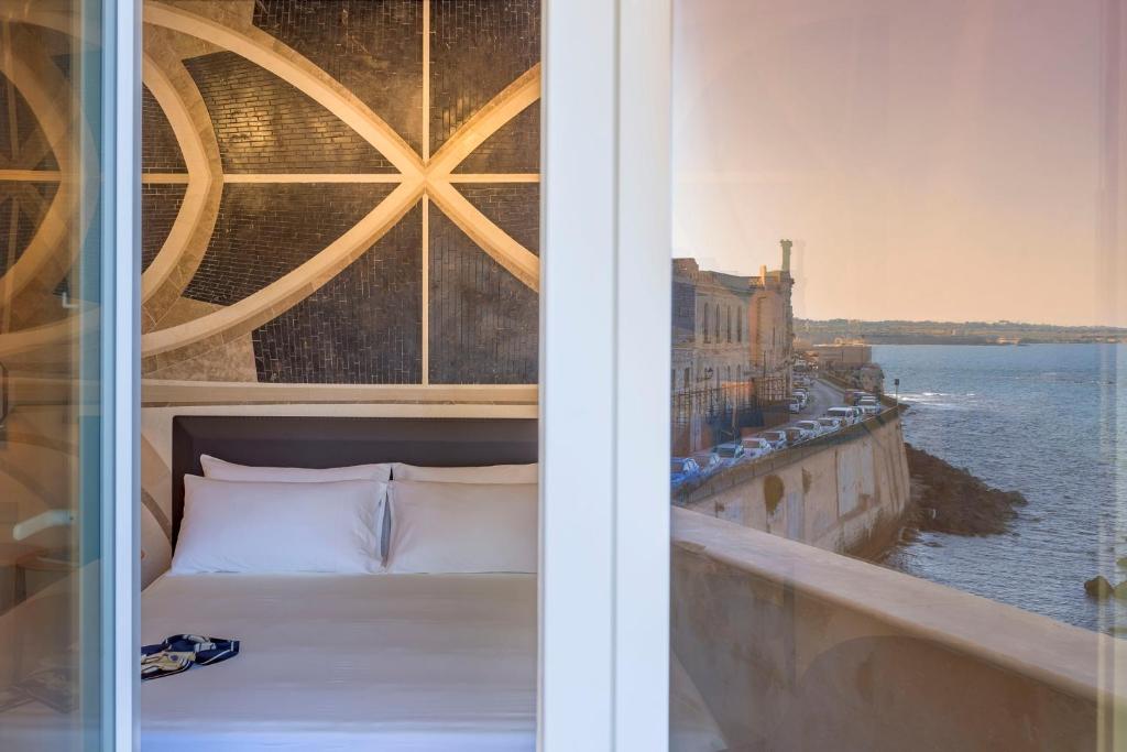 Bett in einem Zimmer mit Blick auf das Wasser in der Unterkunft Maniace Boutique Hotel Ortigia | UNA Esperienze in Syrakus