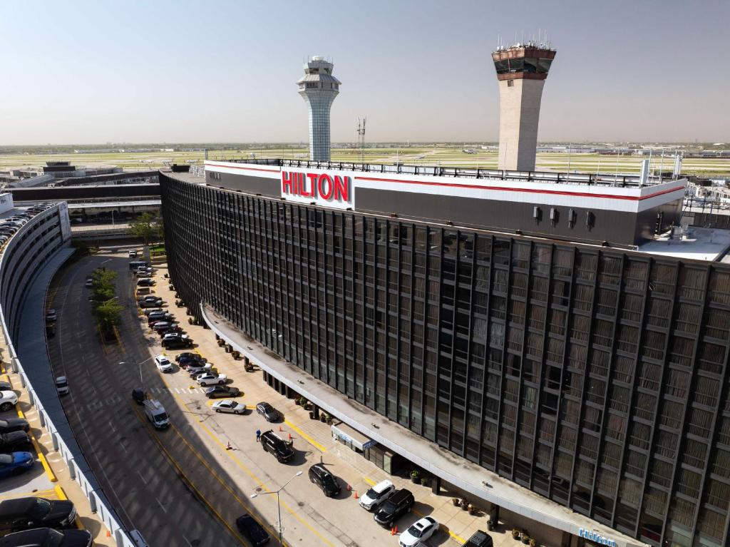 un bâtiment d'aéroport avec des voitures garées dans un parking dans l'établissement Hilton Chicago O'Hare Airport, à Rosemont