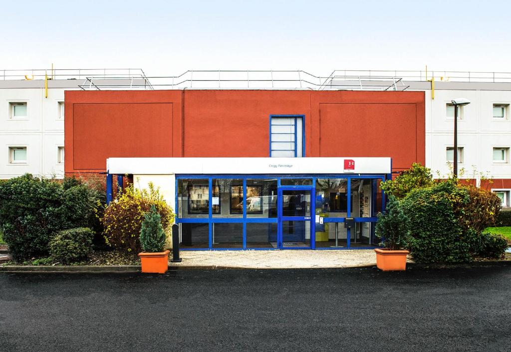 un edificio rosso con una porta blu in un parcheggio di B&B HOTEL Cergy Pierrelaye a Pierrelaye