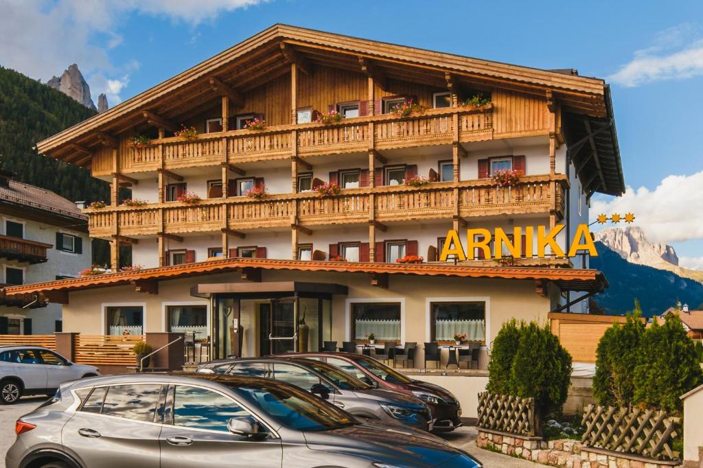 een groot gebouw met auto's geparkeerd voor het bij Hotel Arnika in Pozza di Fassa