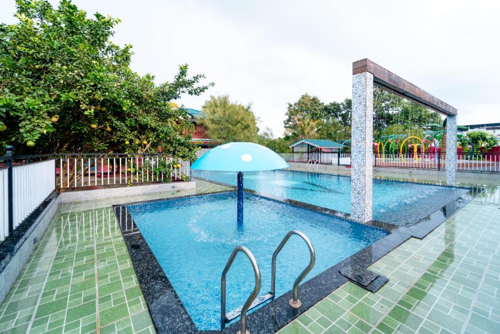 a swimming pool with an umbrella in the middle at Treebo Green Village Resort - Goa in Maneri