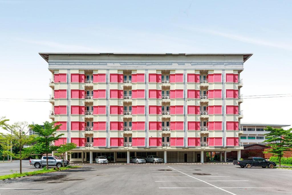 un grand bâtiment rouge avec des voitures garées dans un parking dans l'établissement Capital O VResotel, à Nonthaburi