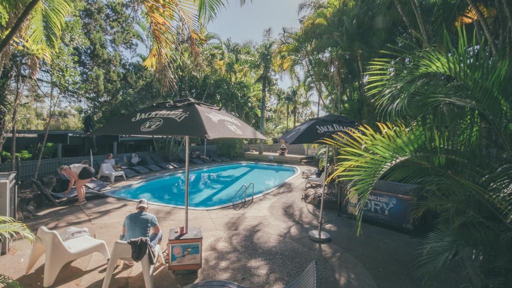 un hombre sentado junto a una piscina con sombrilla en Nomads Noosa, en Noosa Heads