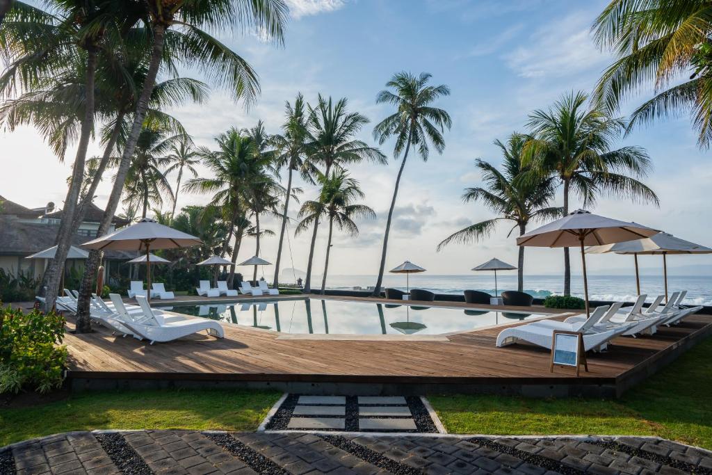 una piscina con sillas y sombrillas y el océano en Nirwana Beach & Resort, en Candidasa