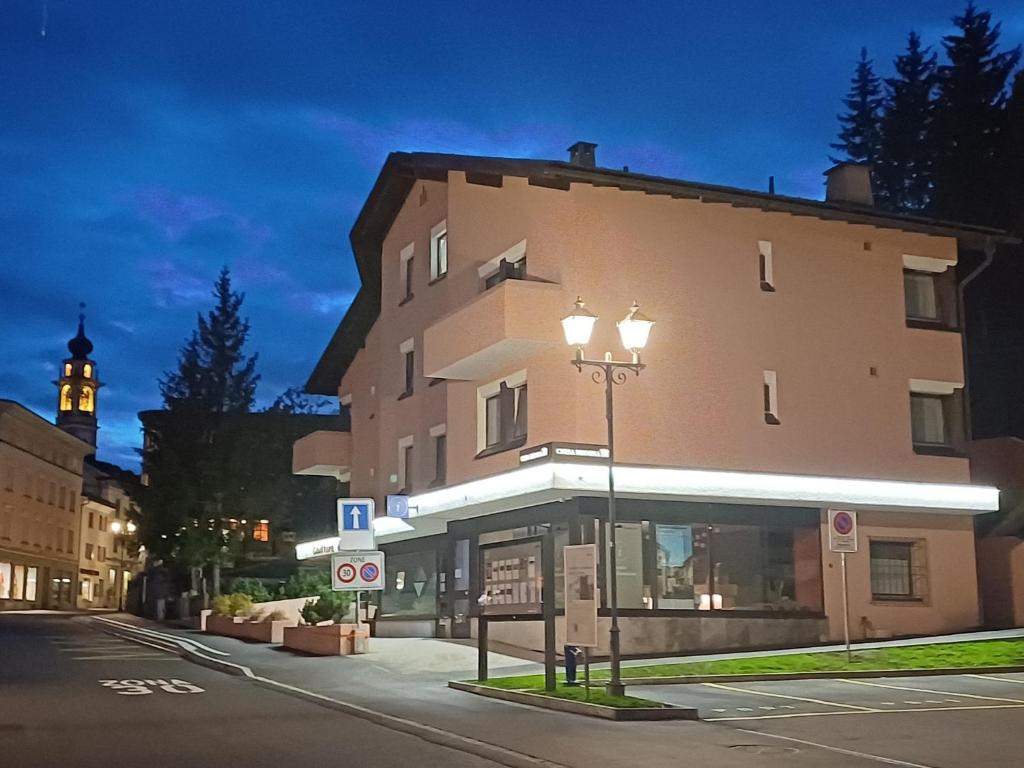 ein Gebäude auf einer Straße mit einem Uhrturm im Hintergrund in der Unterkunft Chesa Bernina in Samedan