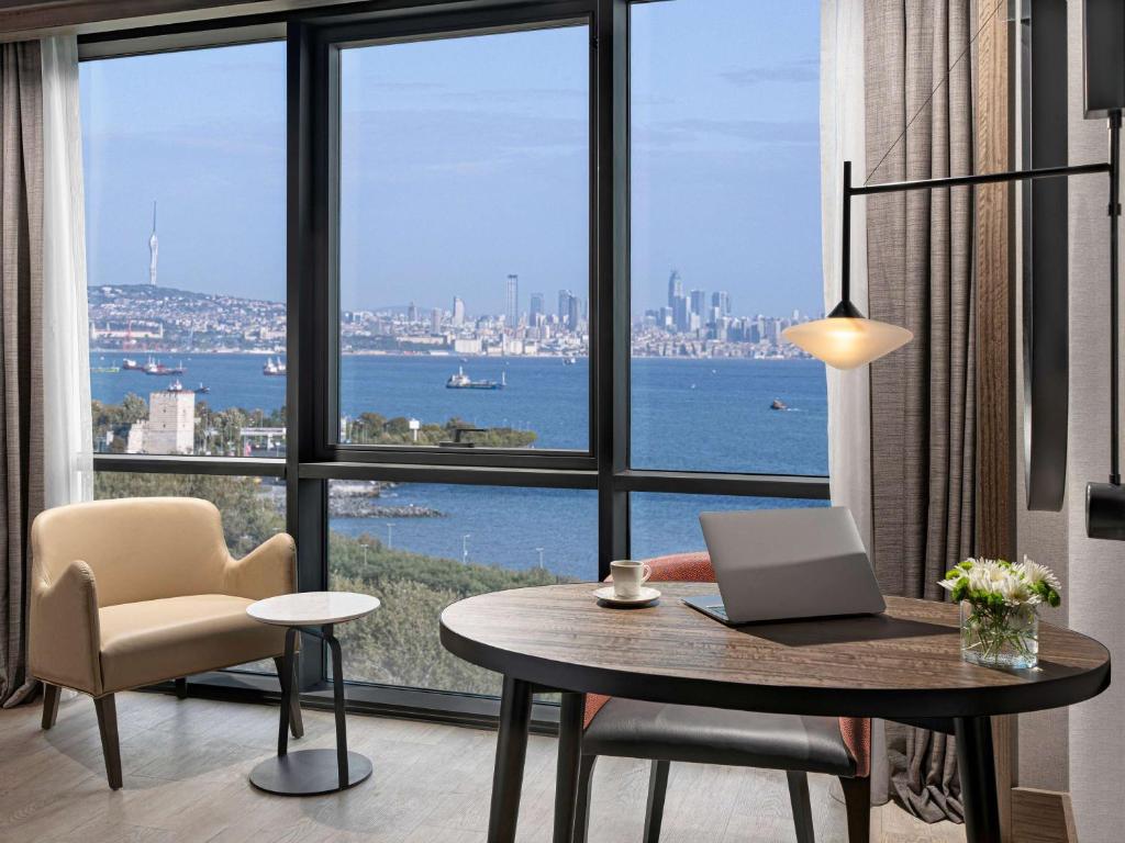 Mövenpick Hotel Istanbul Marmara Sea في إسطنبول: غرفة مع مكتب مع لاب توب ونافذة كبيرة