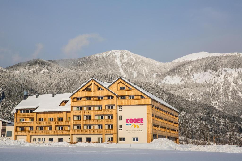 ein großes Gebäude im Schnee mit Bergen im Hintergrund in der Unterkunft COOEE alpin Hotel Dachstein in Gosau