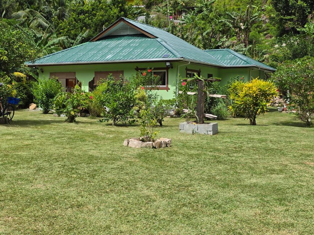 une maison verte avec des arbres et des plantes dans une cour dans l'établissement Dan Zoranz Self Catering Guest House, à La Digue