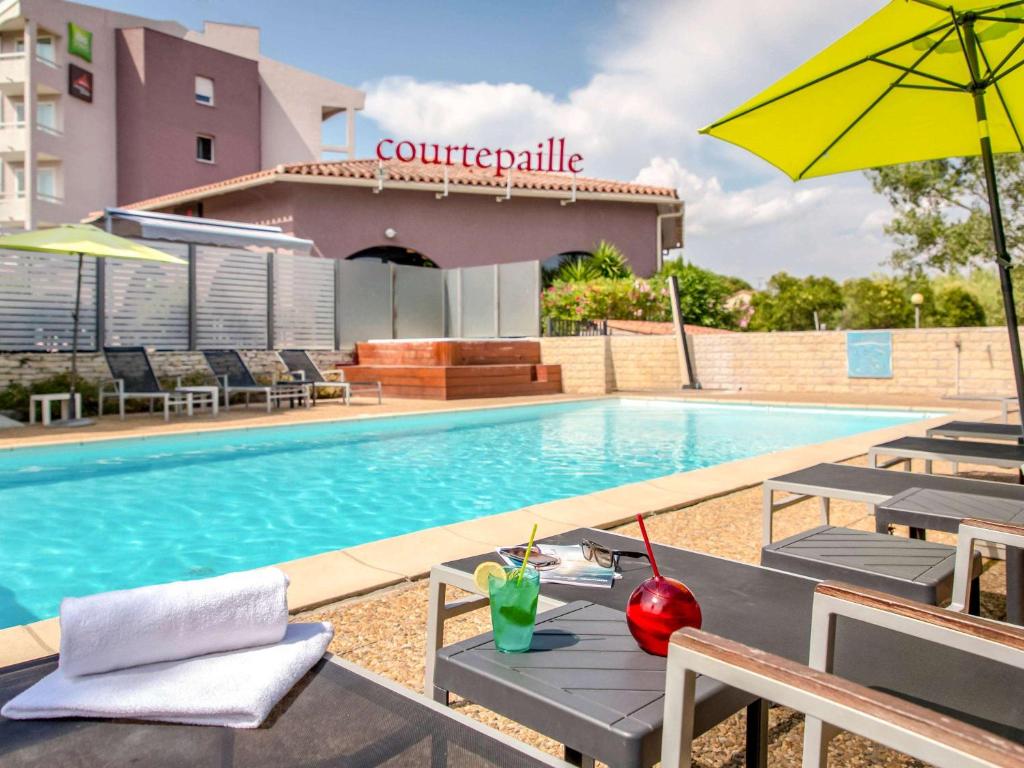 uma piscina com mesa e cadeiras e um guarda-sol em ibis Styles Fréjus St Raphael em Fréjus