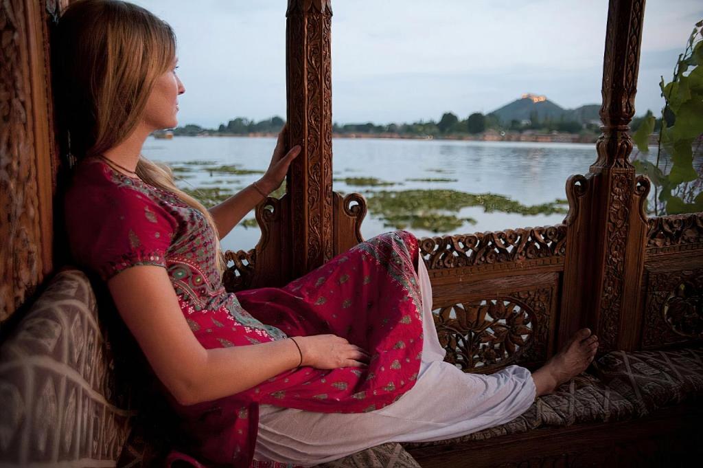 une femme assise sur un lit en regardant l'eau dans l'établissement Heritage Amina Group Of Houseboats, à Srinagar