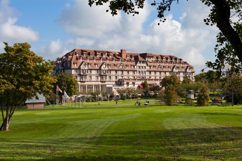 un grande edificio in un parco con un campo verde di Hôtel Barrière L'Hôtel du Golf a Deauville