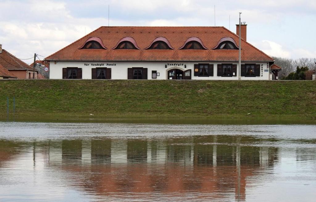 ein Haus mit rotem Dach neben einem Wasserkörper in der Unterkunft Vár Vendéglő Panzió in Sárospatak