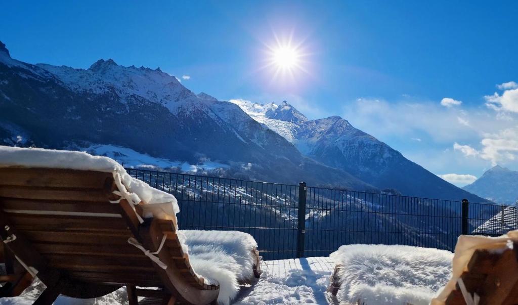 un banco cubierto de nieve con vistas a las montañas en Mattertal Lodge, en Embd