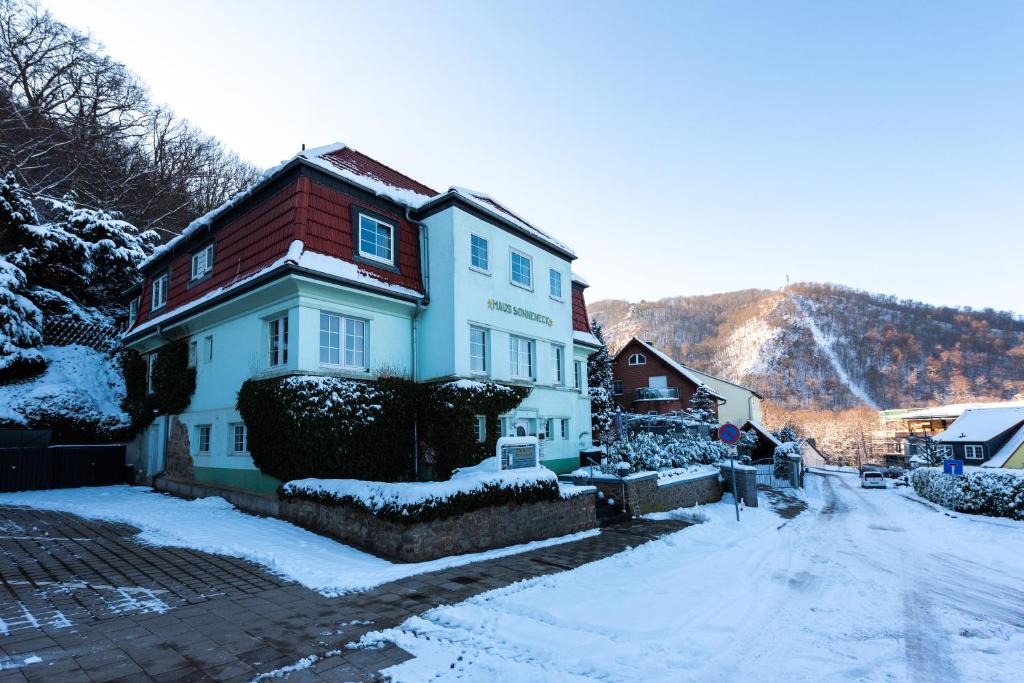 uma casa branca com um telhado vermelho na neve em Hotel Garni Haus Sonneneck em Thale