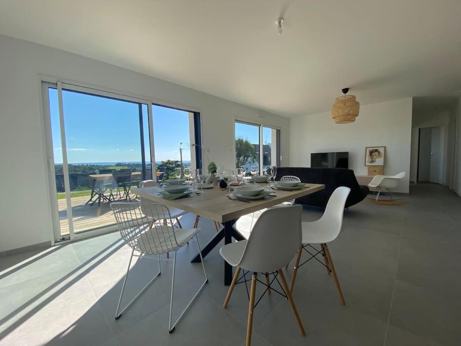 een eettafel en stoelen in een woonkamer met ramen bij Maison neuve vue panoramique sur la mer 6 pers à Crozon in Crozon