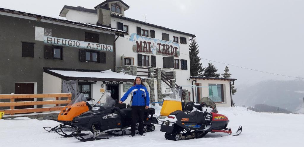 Eine Frau steht neben zwei Schneemobilen im Schnee. in der Unterkunft Rifugio "Mai Tardi" in Madesimo