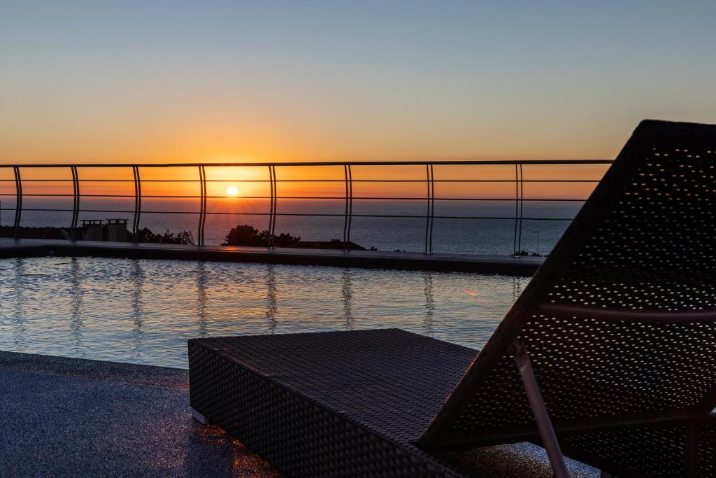 un banc en face d'une piscine avec vue sur le coucher du soleil dans l'établissement Océane Guest House - Adults only, à Nazaré