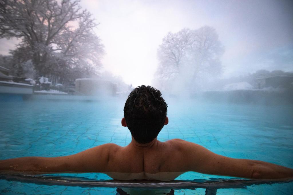 un jeune homme dans une piscine avec une fontaine dans l'établissement Mondorf Parc Hotel & Spa, à Mondorf-les-Bains