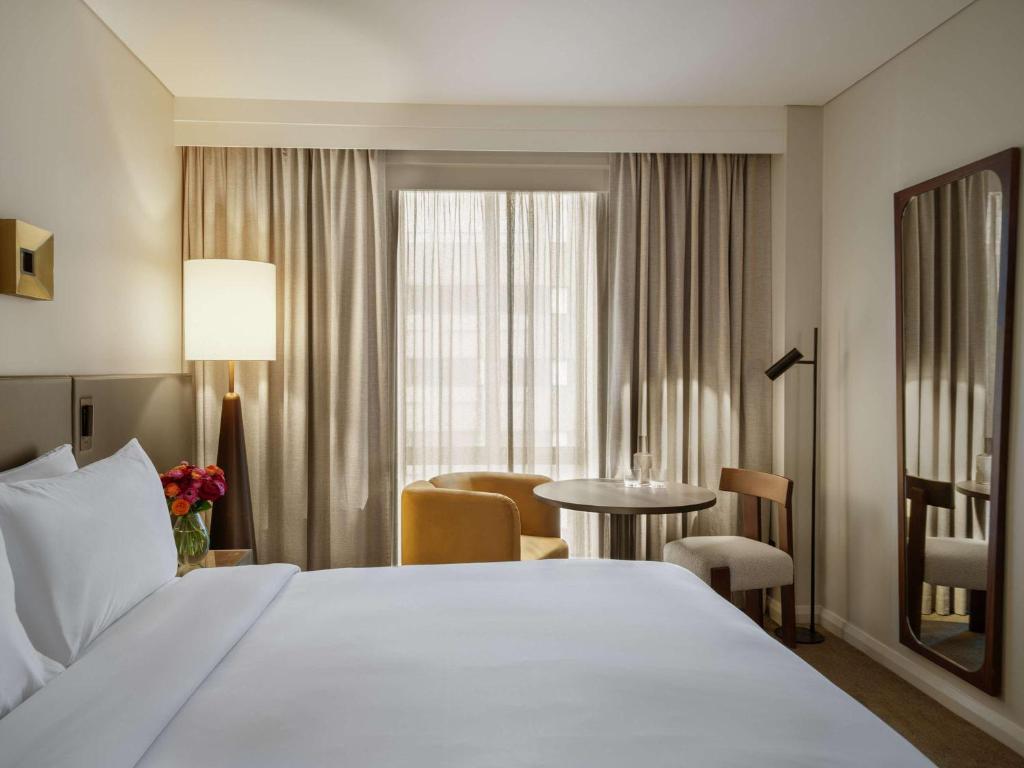 een hotelkamer met een groot wit bed en een tafel bij Sofitel Sydney Wentworth in Sydney