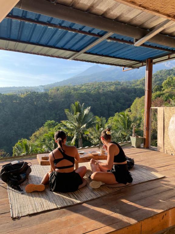 two women in bikinis sitting on a deck with a view at Rinjani Houseboon in Senaru