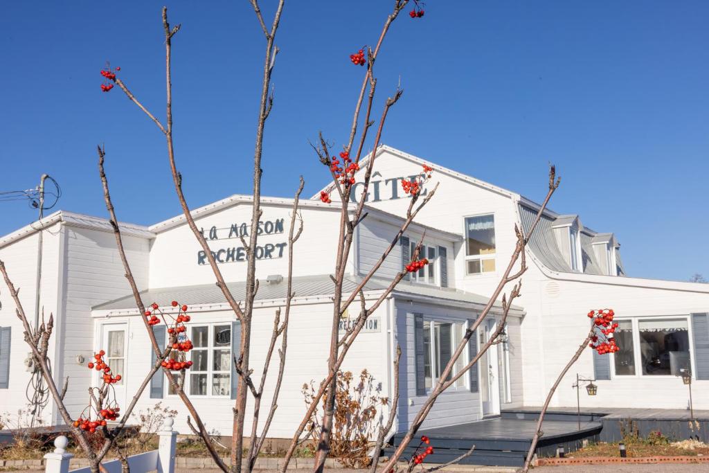 a white house with red flowers in front of it at Gite la Maison Rochefort in Baie-Sainte-Catherine