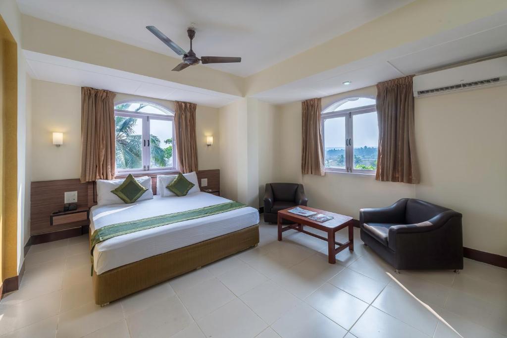 a bedroom with a bed and a chair and windows at Treebo Green Park in Mapusa