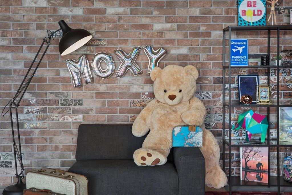 um urso de peluche sentado num sofá ao lado de uma parede de tijolos em Moxy Frankfurt Airport Kelsterbach em Kelsterbach