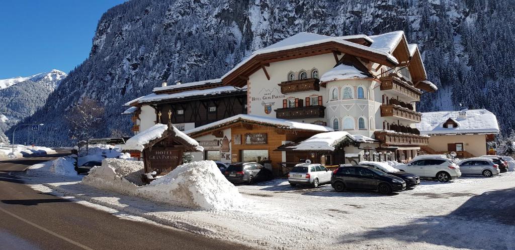 a large building with cars parked in front of a mountain at Hotel Gran Paradis in Campitello di Fassa