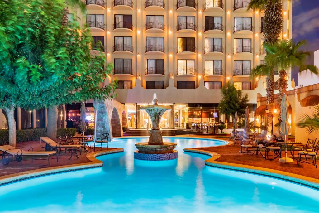 einen Hotelpool mit einem Brunnen vor einem Gebäude in der Unterkunft Hotel Lucerna Ciudad Juarez in Ciudad Juárez