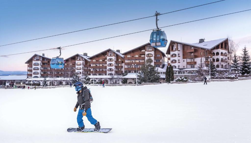 een persoon op een snowboard voor een skihut bij Kempinski Hotel Grand Arena Bansko in Bansko