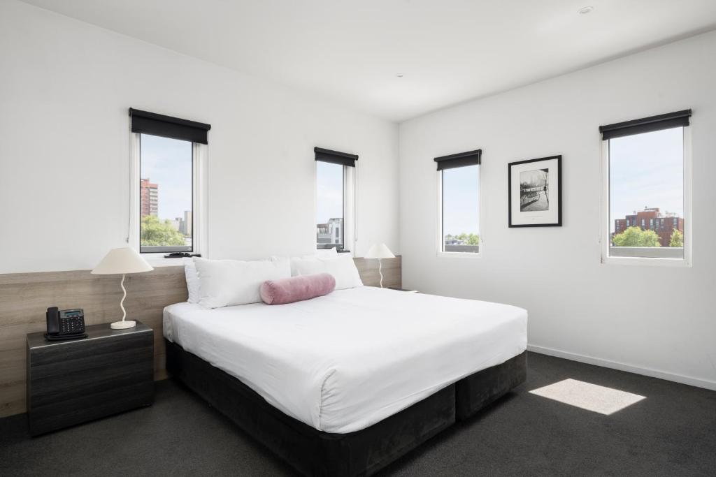 a white bedroom with a large bed and windows at Tyrian Serviced Apartments Fitzroy in Melbourne