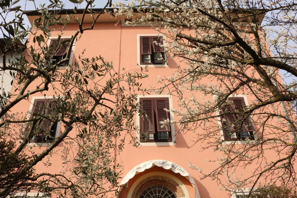 a pink building with three windows and a tree at Angelini in Lucca