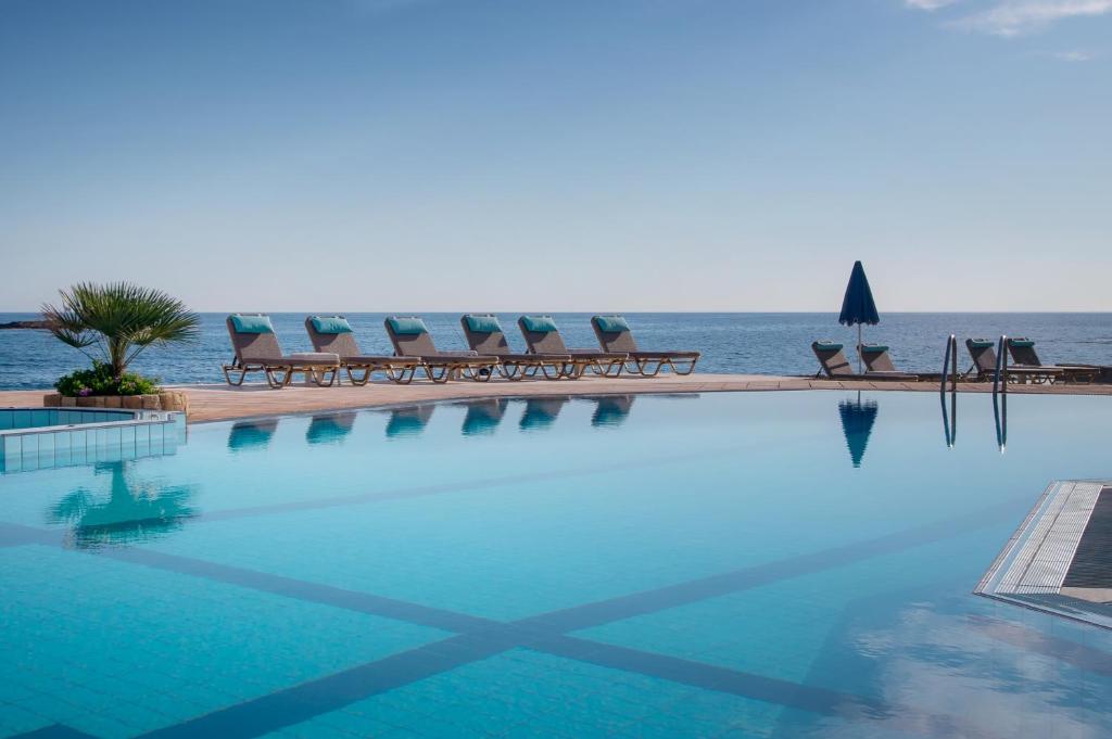 una piscina con sedie e l'oceano sullo sfondo di Pyrgos Beach Hotel Apartments a Mália