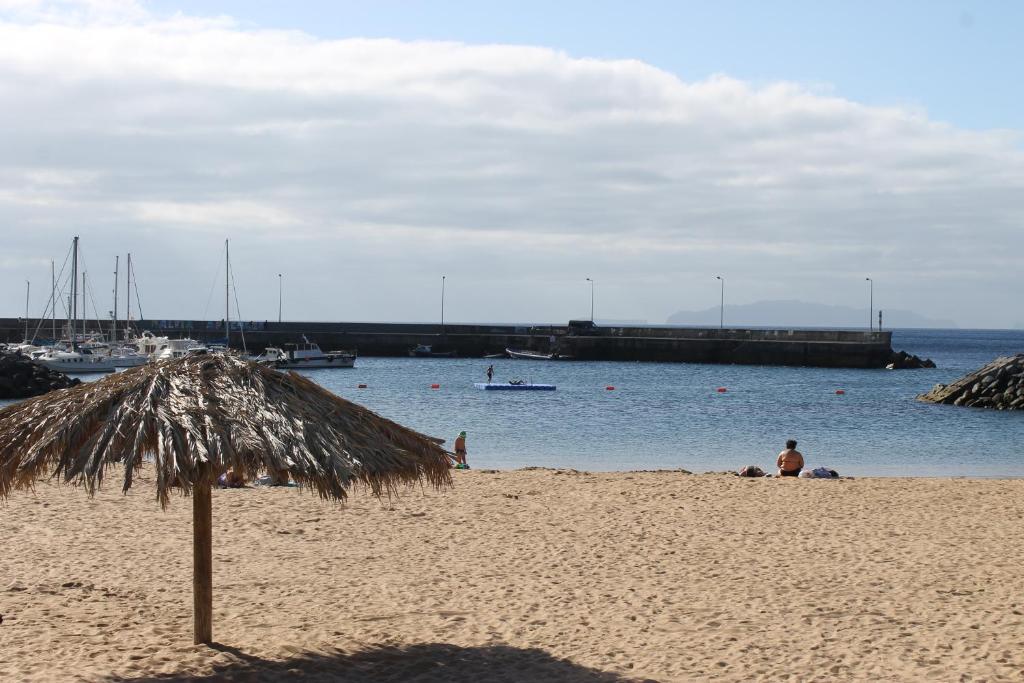 een rieten parasol op een strand met water bij Cozy and Bright Apartment in Machico