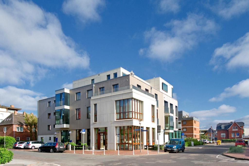 un grand bâtiment blanc avec des voitures garées dans un parking dans l'établissement Hotel Niedersachsen, à Westerland