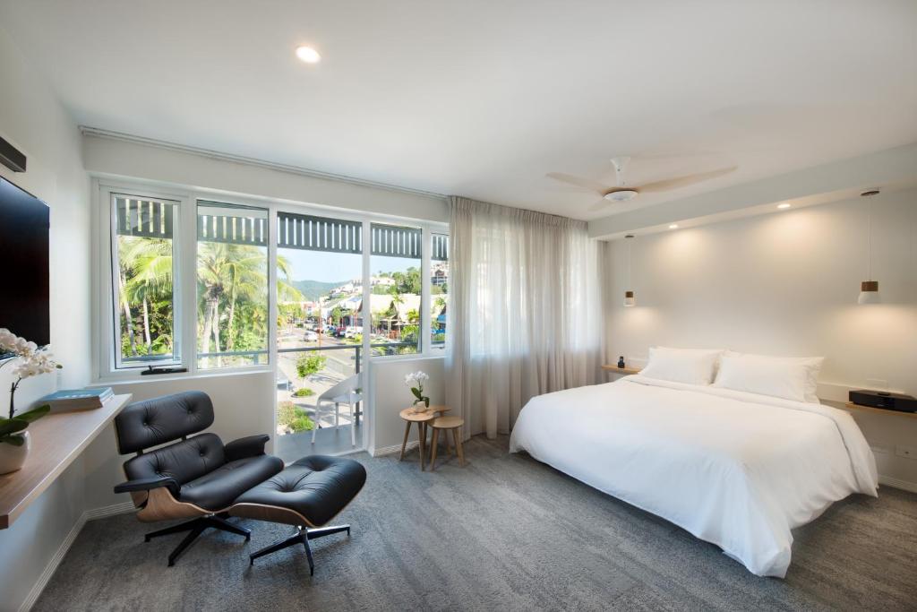 1 dormitorio con cama blanca, silla y ventanas en Heart Hotel and Gallery Whitsundays, en Airlie Beach