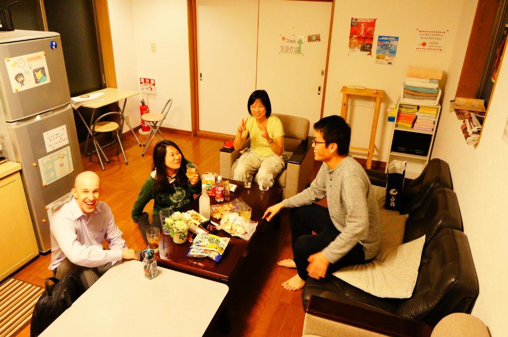 een groep mensen die rond een tafel in een kamer zitten bij Osaka Tomato Guesthouse in Osaka